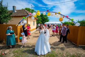 Outdoor wedding celebration with colorful balloon arch decorations against a bright blue sky.