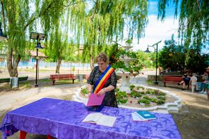 Official ceremony taking place at outdoor table with purple tablecloth under weeping willow trees.