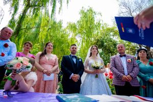 Wedding ceremony participants gather around a decorated purple table under the shade of willow branches.