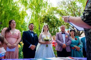 Wedding party and guests assembled in a garden setting with lush green foliage overhead.