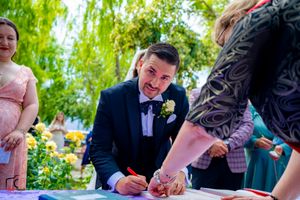 Wedding ceremony signing moment captured in garden setting with willow trees.