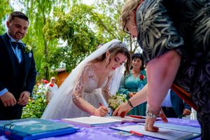 People signing official documents at an outdoor wedding ceremony under green foliage.