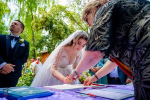 Wedding party members taking turns signing paperwork at a garden ceremony.