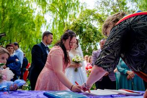 Outdoor wedding signing ceremony with guests watching under weeping willow trees.