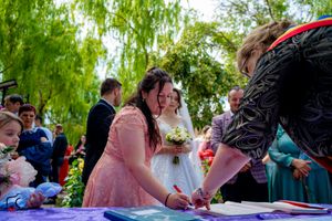 Wedding ceremony participants gathered under trees to sign marriage documents.