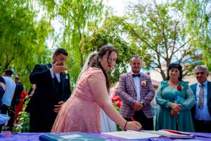 Wedding guests observe document signing during outdoor garden celebration.