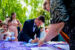 Wedding celebration document signing moment captured under lush green trees.