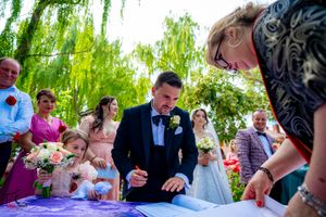 Formal document signing ceremony taking place at outdoor wedding venue.