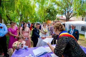 Wedding ceremony participants gather around a registration table decorated in purple under green foliage.