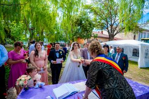 Wedding celebration participants gather around a purple-decorated table for document signing outdoors.