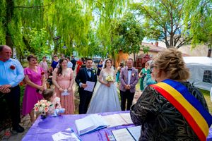 Guests witness marriage document signing at an outdoor ceremony with rainbow sash official.