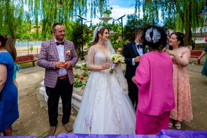 Bridal party enjoying drinks and laughter in a garden setting with willow trees.