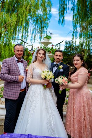 Wedding party members raising glasses in a toast under green willow branches.