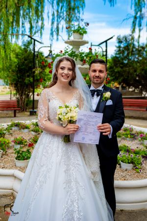 Couple displaying marriage certificate in beautiful garden with weeping willows.