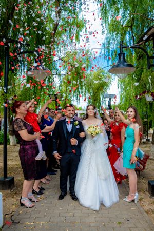 Joyful wedding scene with guests throwing red petals as couple walks down brick pathway.