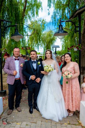 Wedding party poses together on brick pathway with willow trees in background.