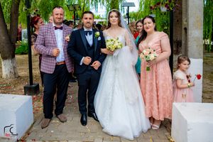 Wedding group photo with bridal party in formal attire on brick walkway.
