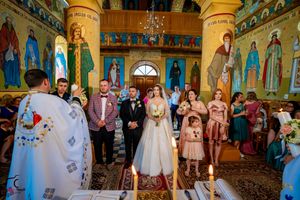 Wedding ceremony in progress inside an elaborately decorated Orthodox church with painted murals.