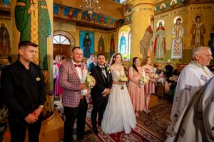 Wedding service taking place in a traditional Orthodox church with golden walls and religious artwork.