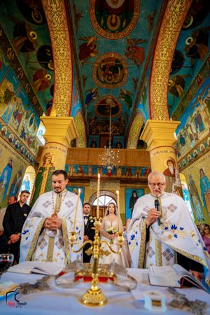 Orthodox priests conduct a religious ceremony inside an ornate church with golden decorations and painted ceiling.