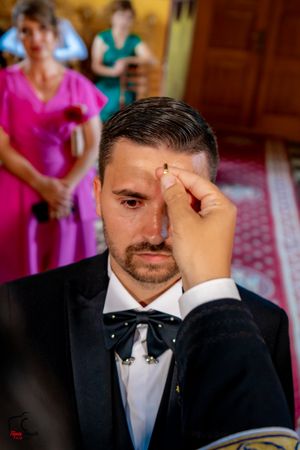 Orthodox wedding ceremony participant receiving blessing with attendees in background.
