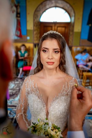 Bride wearing sparkly lace wedding dress holding white bouquet in church setting.