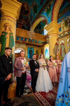 Orthodox church interior with golden columns and painted religious scenes hosts a wedding ceremony.