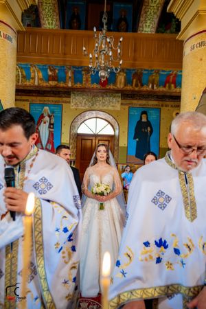 Orthodox wedding ceremony in an ornate church with priests in white embroidered robes and religious icons on the walls.