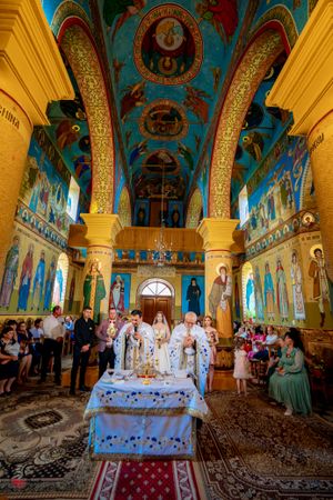 Ornate Orthodox church interior with blue ceiling, golden columns and religious murals during a ceremony.