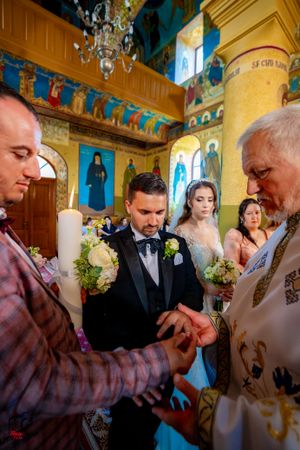 Religious ceremony in progress inside an Orthodox church with decorated walls and chandelier.