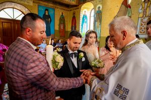 Wedding ceremony participants gathered around priest during traditional Orthodox service.