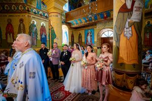 Orthodox wedding ceremony in an ornate church with gold details and religious iconography on the walls.