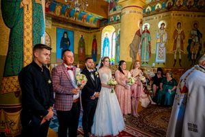 Panoramic view of a wedding ceremony in an Orthodox church with decorative murals and golden columns.