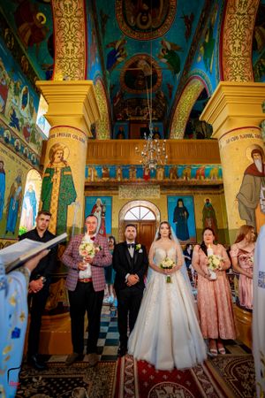 Wedding party gathered in an ornate Orthodox church with turquoise and gold architectural details.