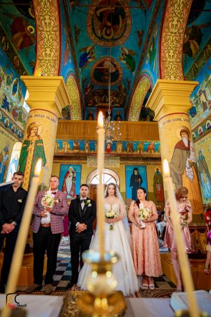 Wedding party standing beneath ornate church ceiling with golden columns and religious artwork during ceremony.