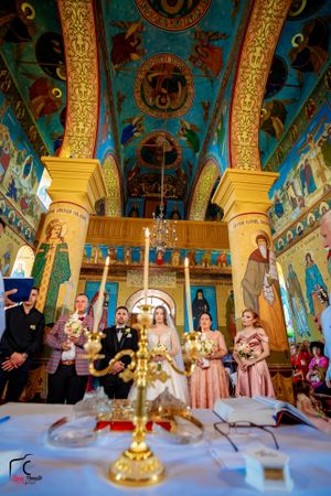 Orthodox wedding ceremony in an ornate church with vibrant blue ceiling and golden columns featuring religious iconography.