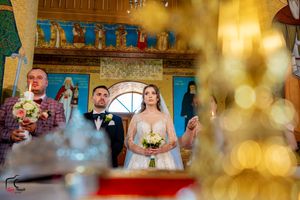 Wedding ceremony through decorative foreground elements in an Orthodox church with painted walls.