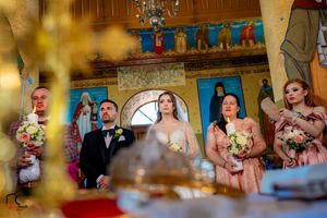 Wedding party viewed through golden decorative elements in traditional Orthodox church setting.