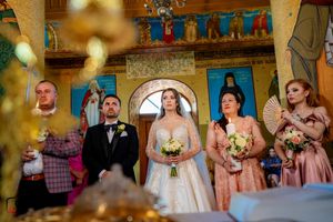 Wedding ceremony participants standing in front of religious icons in an Orthodox church interior.