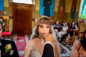 Traditional Orthodox wedding ceremony with crowns being held over couple's heads in decorated church.