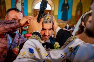 Orthodox priest conducting marriage ceremony with traditional crowns in decorated church setting.