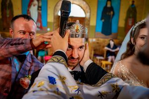 Wedding ceremony participants gathered near iconostasis in Orthodox church with golden details.