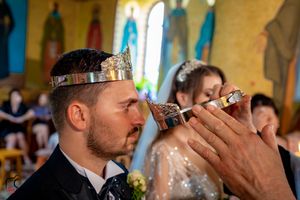 Wedding couple participates in traditional Orthodox drinking ceremony inside decorated church.