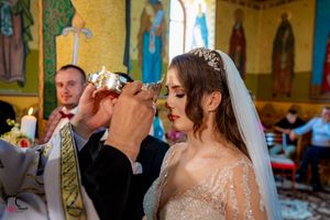 Wedding ceremony participants share ritual drink in beautifully decorated Orthodox church.