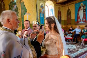 Orthodox wedding ritual performed in church with golden murals and decorative elements.