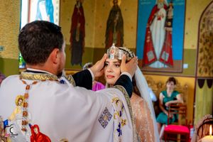 Traditional Orthodox marriage ceremony with priest performing rituals in decorated church interior.