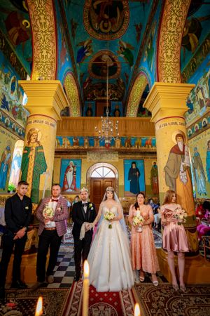 Wedding ceremony in an ornate Orthodox church with blue and gold decor and religious icons adorning the walls.