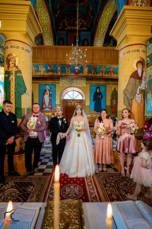 Orthodox wedding ceremony taking place in a beautifully decorated church with golden columns and vibrant frescoes.