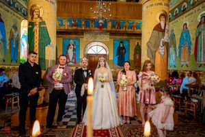 Orthodox church wedding ceremony with attendants standing beneath ornate frescoes and gilded decorations.