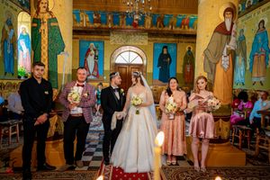Panoramic view of a wedding celebration inside an Orthodox church featuring intricate wall paintings and columns.